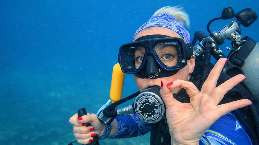 Diver underwater with snorkeling gear and scuba tank, making peace sign at Warwick Le Lagon - Vanuatu, Efate.