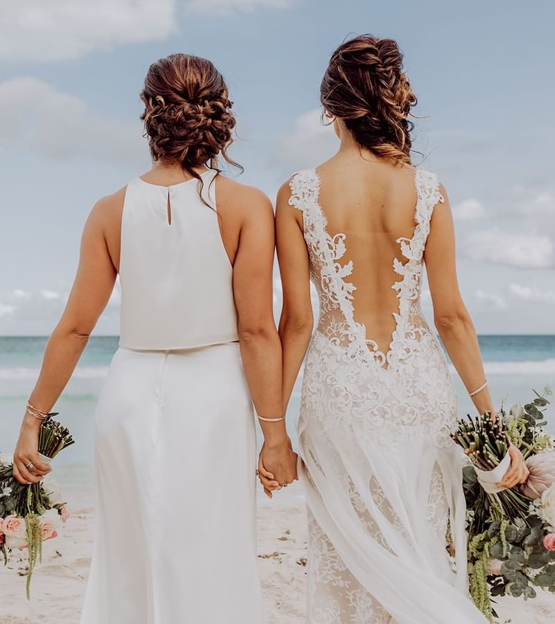 2 brides holding hands on the beach at Mundo Imperial