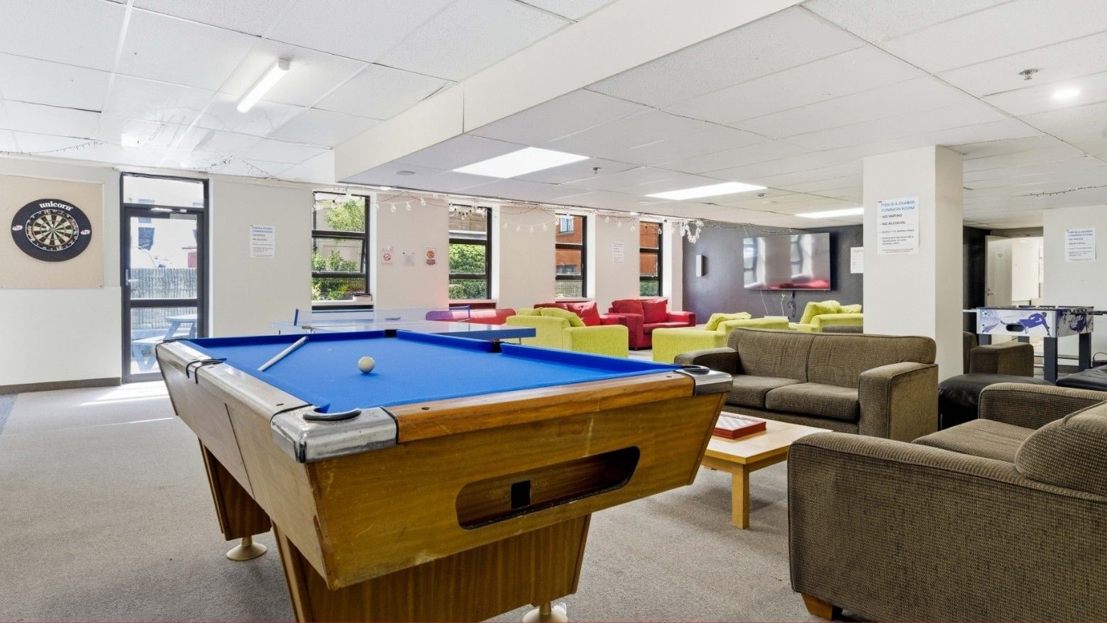 Pool table with cue and ball in a room with couches and a dartboard.