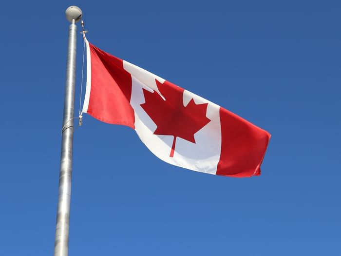 Canadian flag waving on a silver pole against a clear, bright blue sky near Coast Dawson Creek Hotel