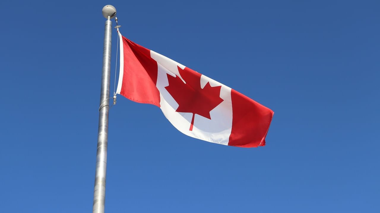 Canadian flag waving on a silver pole against a clear blue sky.