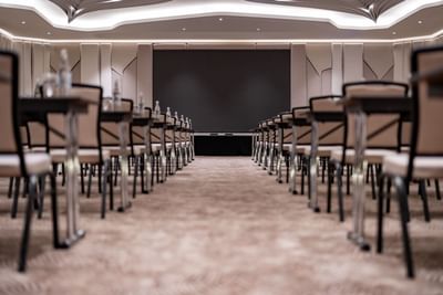 Classroom table arrangement with carpeted floors & a screen in the Meeting Room at Amora Hotel