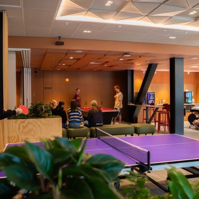 Guests playing table tennis in a modern recreation area with pool table and lounge seating at Tupuārangi