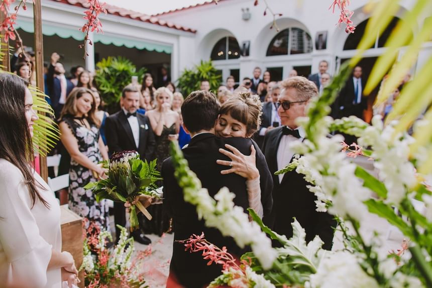 Emotional outdoor wedding ceremony hug between the bride and groom, surrounded by guests at Tradewinds Apartment Hotel