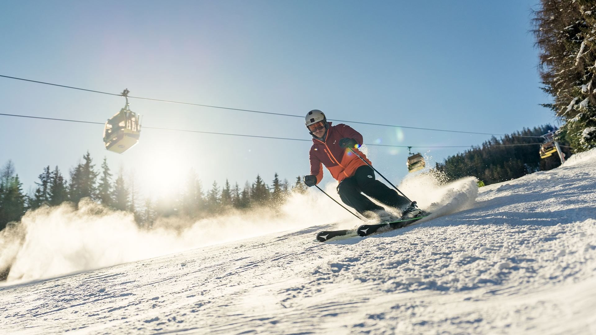 Skier descending snowy slope with ski lift in background at Falkensteiner Hotel Schladming