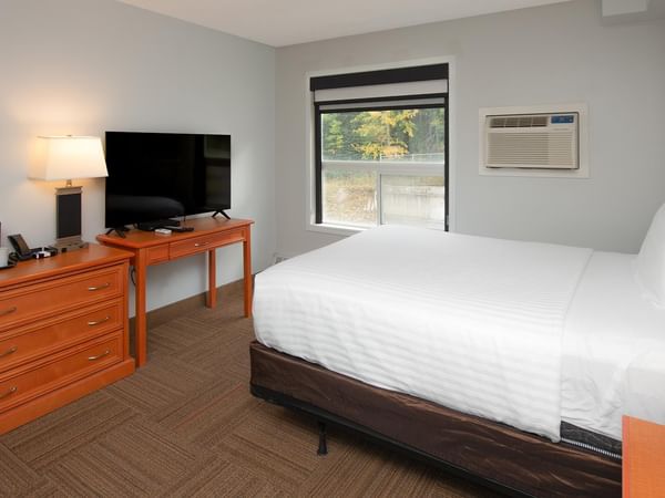 Coast Queen with Kitchenette featuring white bedding, wooden dresser and window view.