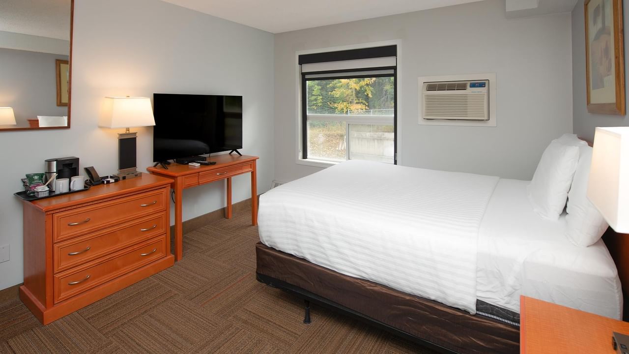 Coast Queen with Kitchenette featuring white bedding, wooden dresser and window view.