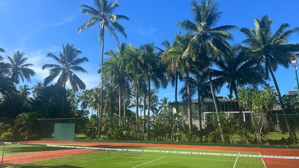 Tennis courts surrounded by lush greenery and palm trees at Warwick Fiji Resort and Spa in Korolevu.
