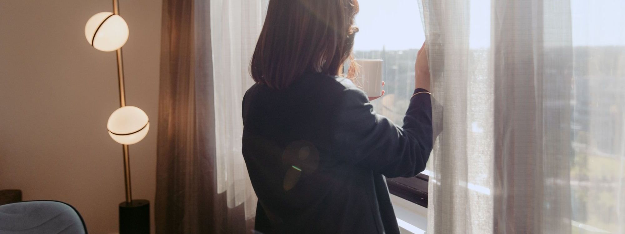 Woman enjoying a room view with a cup in hand in a hotel room.
