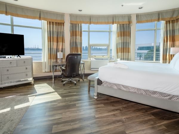 Coast Waterfront Suite with large windows, a bed, a desk, TV, and a view of the city at Coast Lonsdale Quay Hotel
