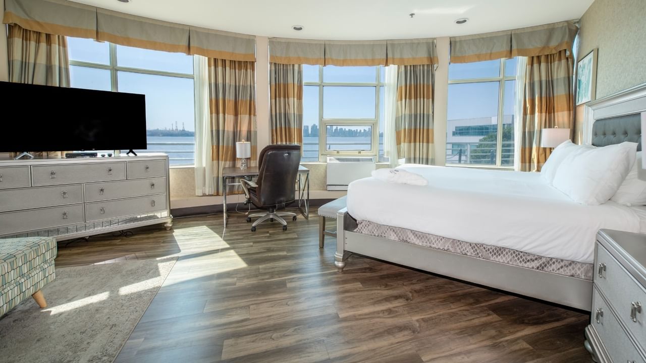 Coast Waterfront Suite with large windows, a bed, a desk, TV, and a view of the city at Coast Lonsdale Quay Hotel