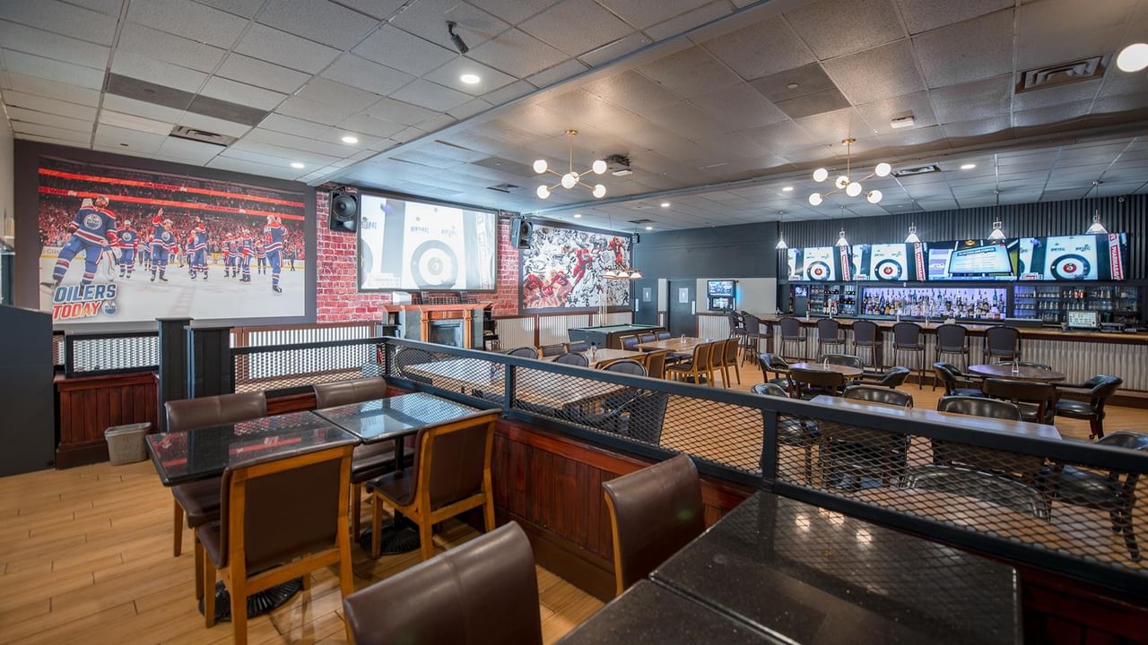 Interior of The Den Pub with tables, chairs, and TVs playing sports.
