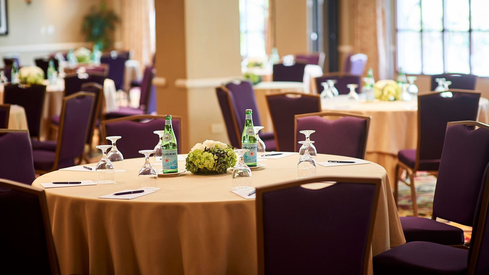 Banquet hall with round tables, purple chairs, floral centerpieces, and bottles of water.