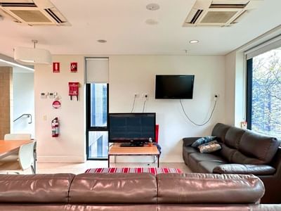 Living room with couches, dining area, TV, and large windows at La Trobe University - McFarlane's Hill Residences.