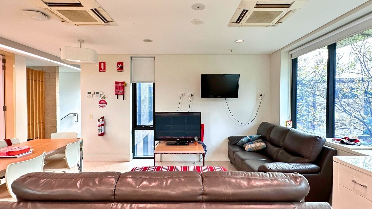 Living room with couches, dining area, TV, and large windows at La Trobe University - McFarlane's Hill Residences.