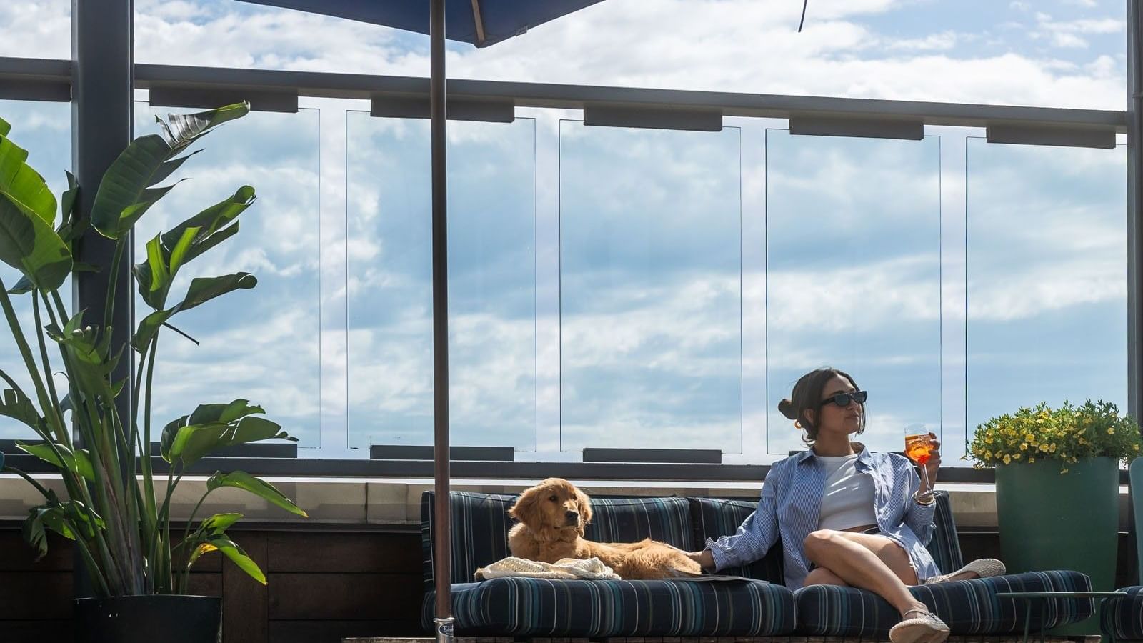Woman enjoying a cocktail, relaxing with puppy under umbrella at Gansevoort Meatpacking NYC, offering luxury NYC hotel deals