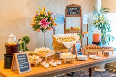 Coffee break set-up with snacks, beverages, floral arrangement, and a chalkboard sign at Hotel Los Delfines & Casino