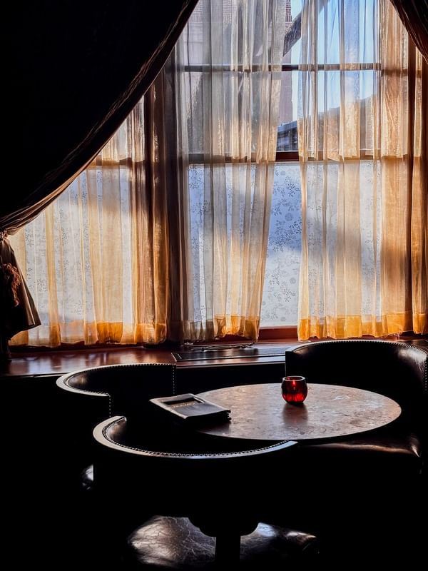 Glass candle holders by a dark table under a large window with gold curtains in The Library at Warwick Melrose Dallas