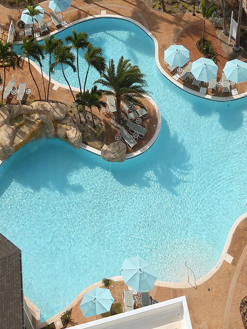 View of Warwick Paradise Island Bahamas, a large pool by white umbrellas under palm trees surrounding a tropical harbor