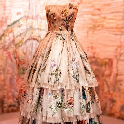 Eine ausgestellte, blumenbestickte, weiße, bodenlange Robe vor einem orangefarbenen Hintergrund.