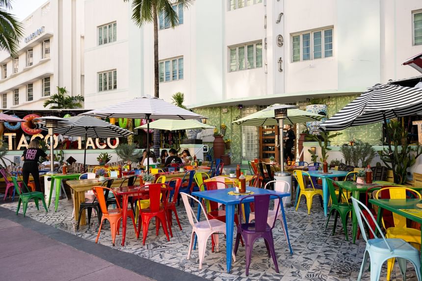 Colorful outdoor dining patio with multicolored chairs and tables beneath striped umbrellas at Riviera Hotel South Beach