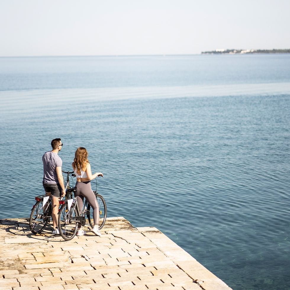Two people with bicycles near water at the edge of a pier.