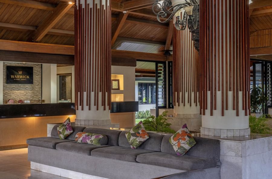 Cozy lobby lounge area with a grey sectional sofa and vibrant floral-patterned cushions at warwick le lagon-vanuatu