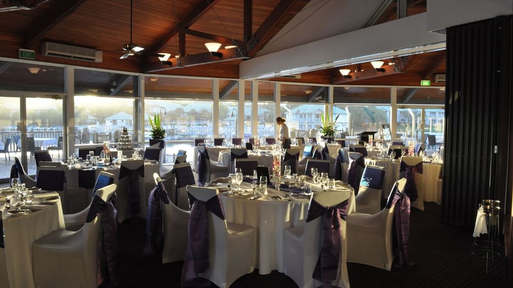Banquets with glassware by large windows overlooking a waterfront in Lily’s on the Lagoon at Novotel Sunshine Coast Resort