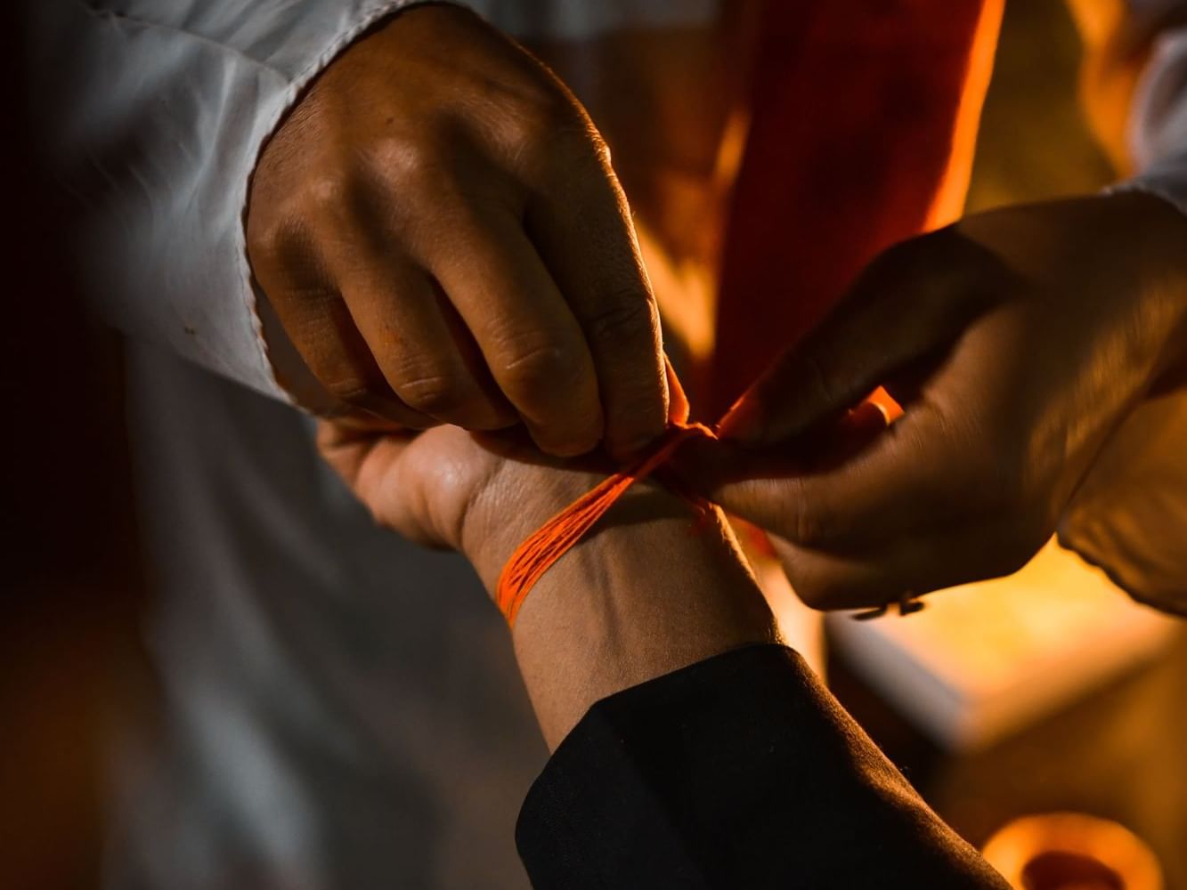 Two hands tie a ceremonial red thread around a wrist during a traditional ritual near Dwarika's Himalayan Wellbeing