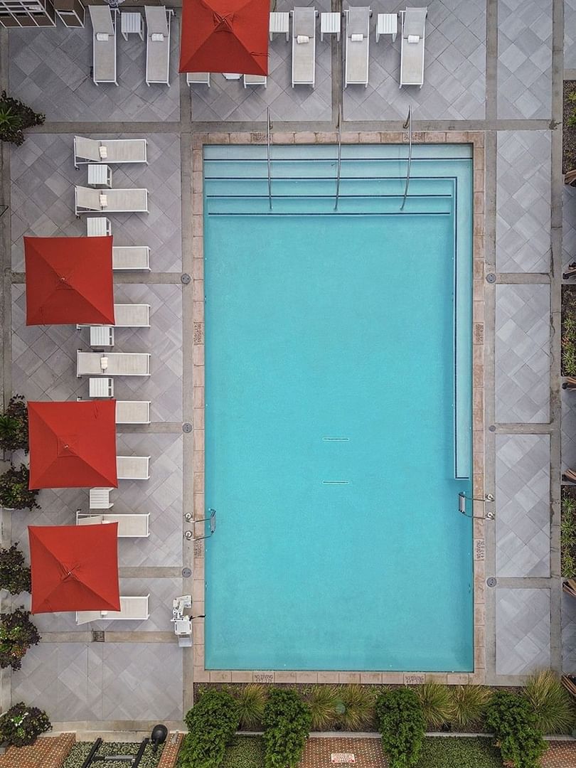 Blue pool by lounge chairs under red umbrellas surrounding the outdoor terrace at Warwick Melrose Dallas