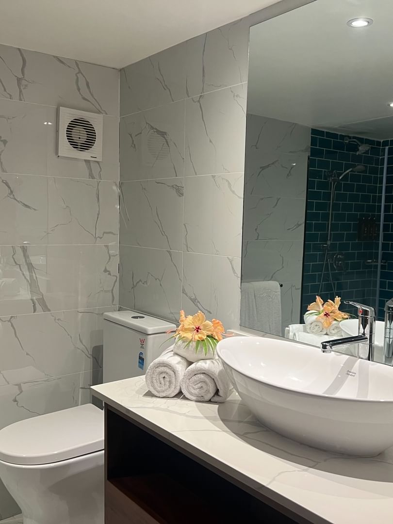 White oval vessel sink by rolled towels and a red flower under a large mirror at Warwick Hotels & Resorts