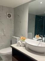 White oval vessel sink by rolled towels and a red flower under a large mirror at Warwick Hotels & Resorts