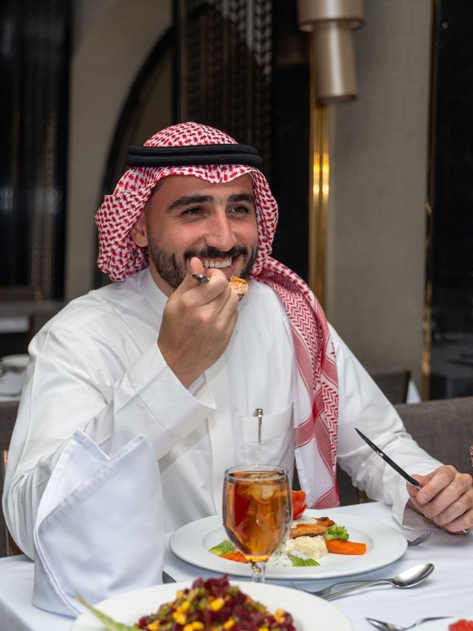 Smiling man in a ghutra eating a gourmet meal at a fine dining  in Al Duhaa restaurant at Saja Warwick Madinahat Saja Warwick Madinah