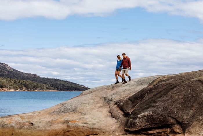 Landscape view of a couple strolling down a rock by the Bay near Freycinet Lodge