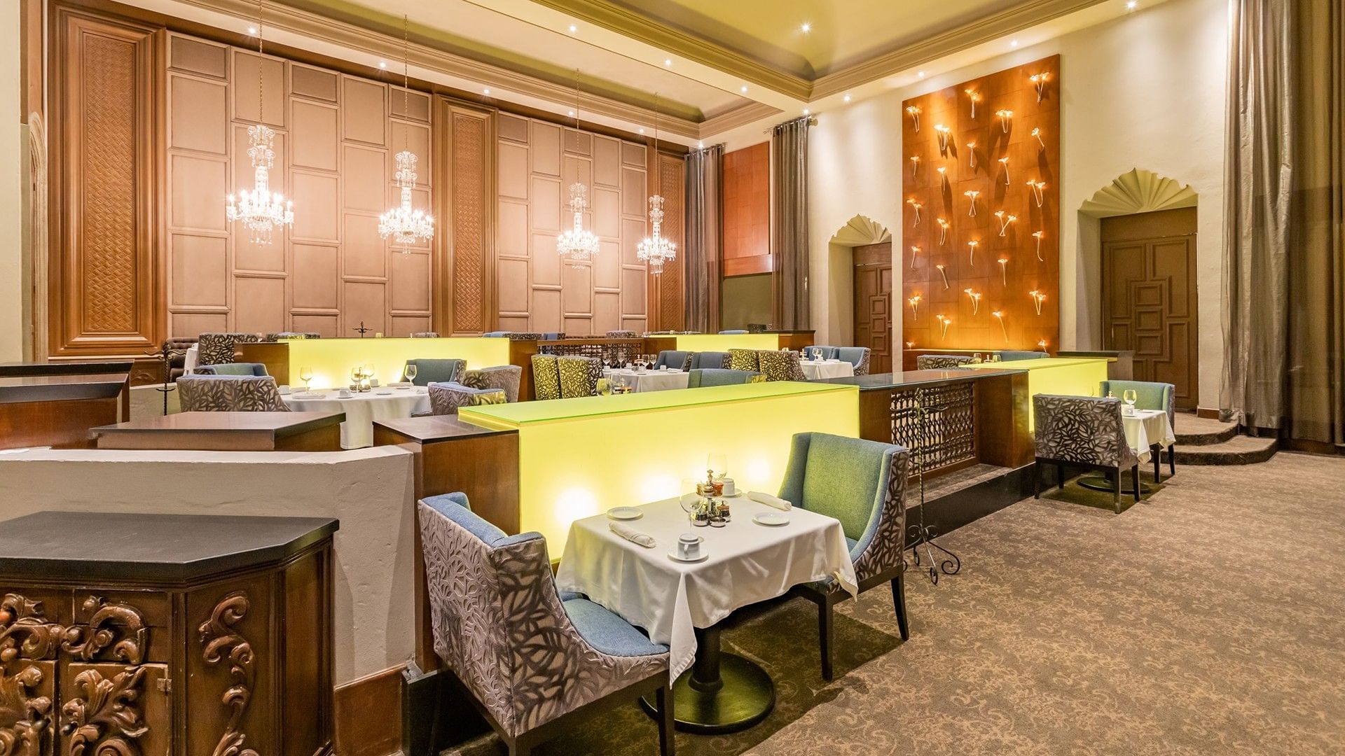 Tierra Mía restaurant showing glowing yellow partitions and crystal chandeliers overhead at Quinta Real Monterrey