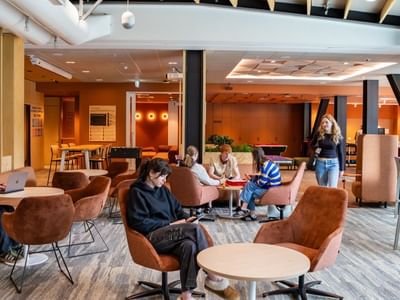 Modern communal lounge with warm wood accents, brown chairs, and guests working at Tupuārangi