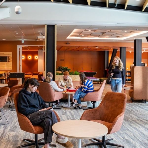 Modern communal lounge with warm wood accents, brown velvet chairs, and guests working at Tupuārangi