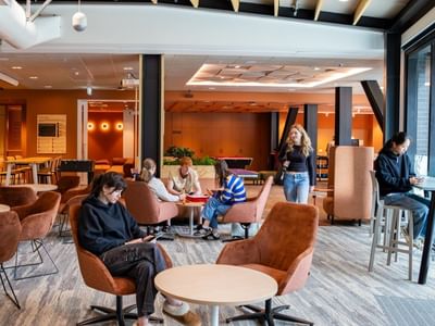 Modern communal lounge with warm wood accents, brown velvet chairs, and guests working at Tupuārangi