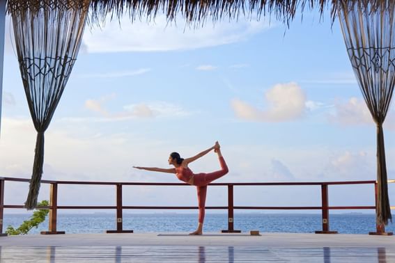 Woman doing yoga on seaside deck at Grand Park Kodhipparu, Maldives