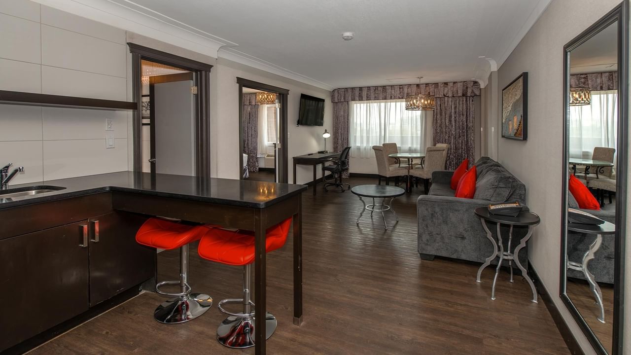 Spacious suite with kitchenette, red bar stools, gray sofa, dining area, and dark wood floors at Coast Calgary University Area Hotel by APA