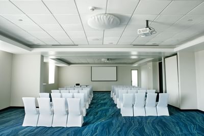 Conference room with rows of chairs, projector and screen at D Sabana Hotel