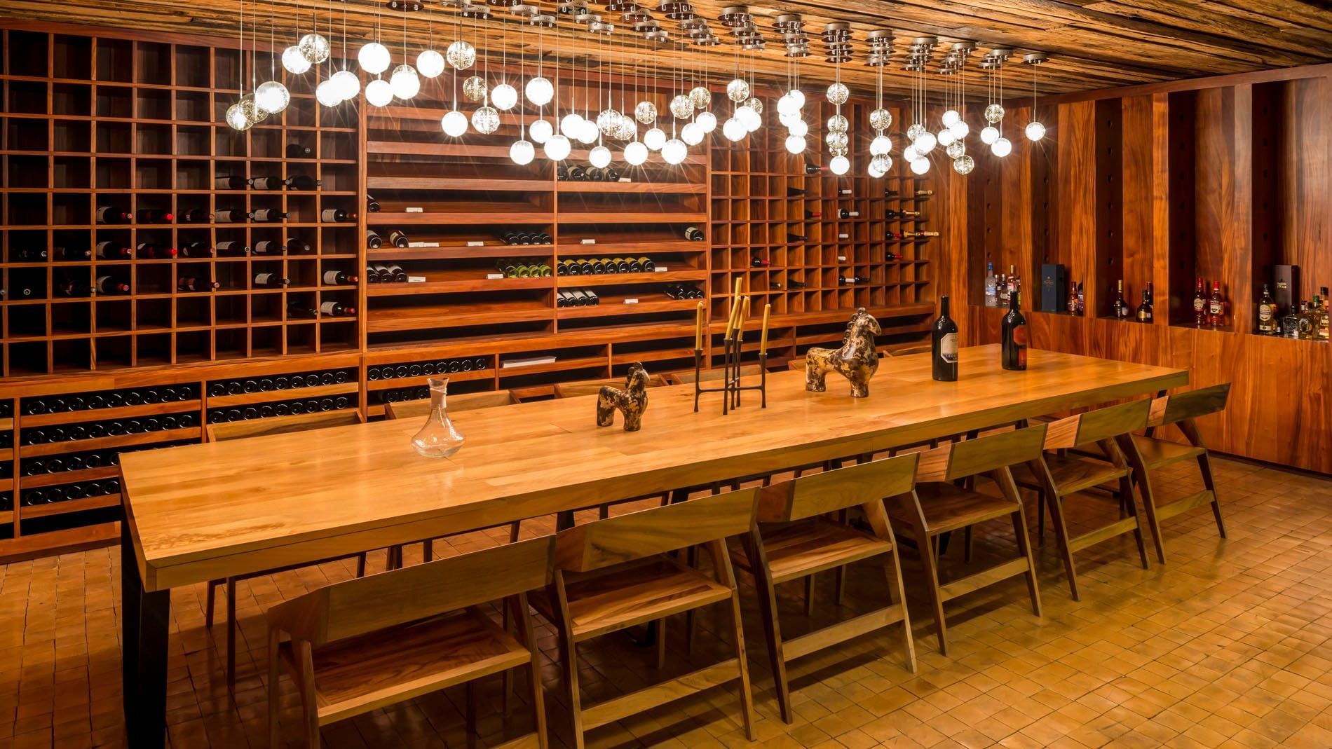 Elegant wine cellar in Blue Bar with a long wooden table and warm hanging lights at Camino Real Puebla Angelopolis