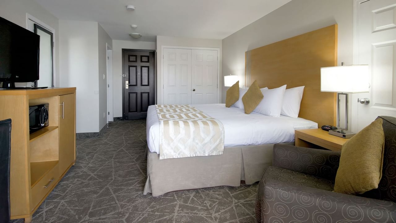 Hotel room with a king-sized bed, beige headboard, patterned armchair and a TV stand.