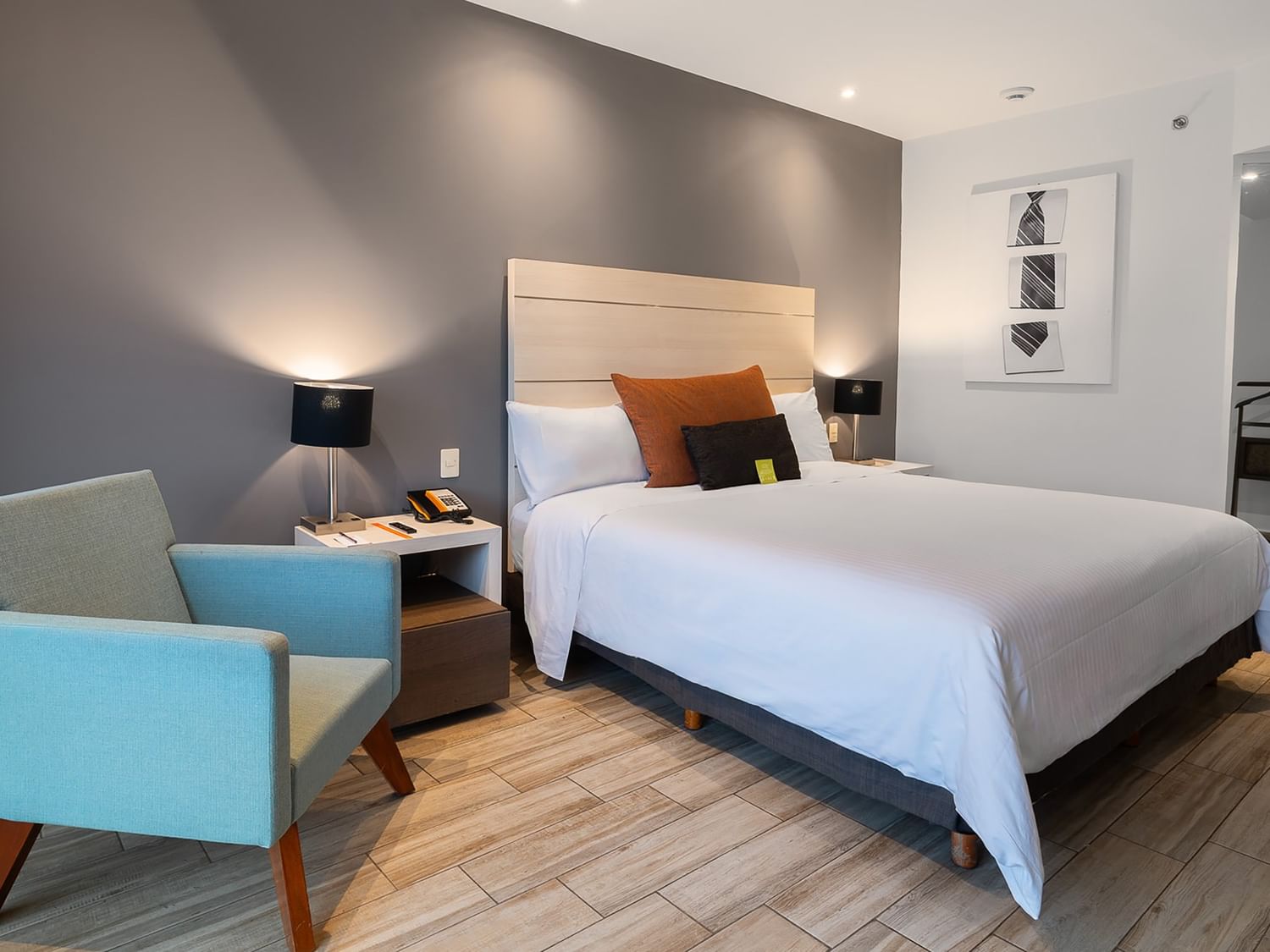 Habitación de lujo king con cama grande, silla azul y piso de madera en Real Inn Perinorte Tlalnepantla.