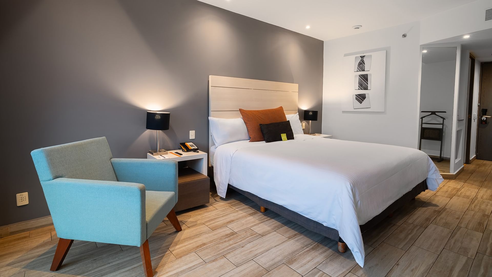 Habitación de lujo king con cama grande, silla azul y piso de madera en Real Inn Perinorte Tlalnepantla.