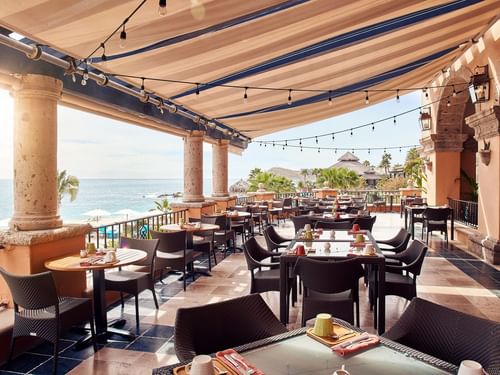 Tomates restaurant terrace with empty tables, sunlit views, and a thatched roof palapa at Hacienda del Mar Los Cabos.
