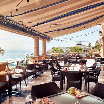 Trattoria Pomodoro terrace with empty tables, sunlit views, and a thatched roof palapa at Hacienda del Mar Los Cabos.