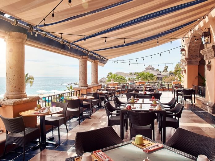 Trattoria Pomodoro terrace with empty tables, sunlit views, and a thatched roof palapa at Hacienda del Mar Los Cabos.