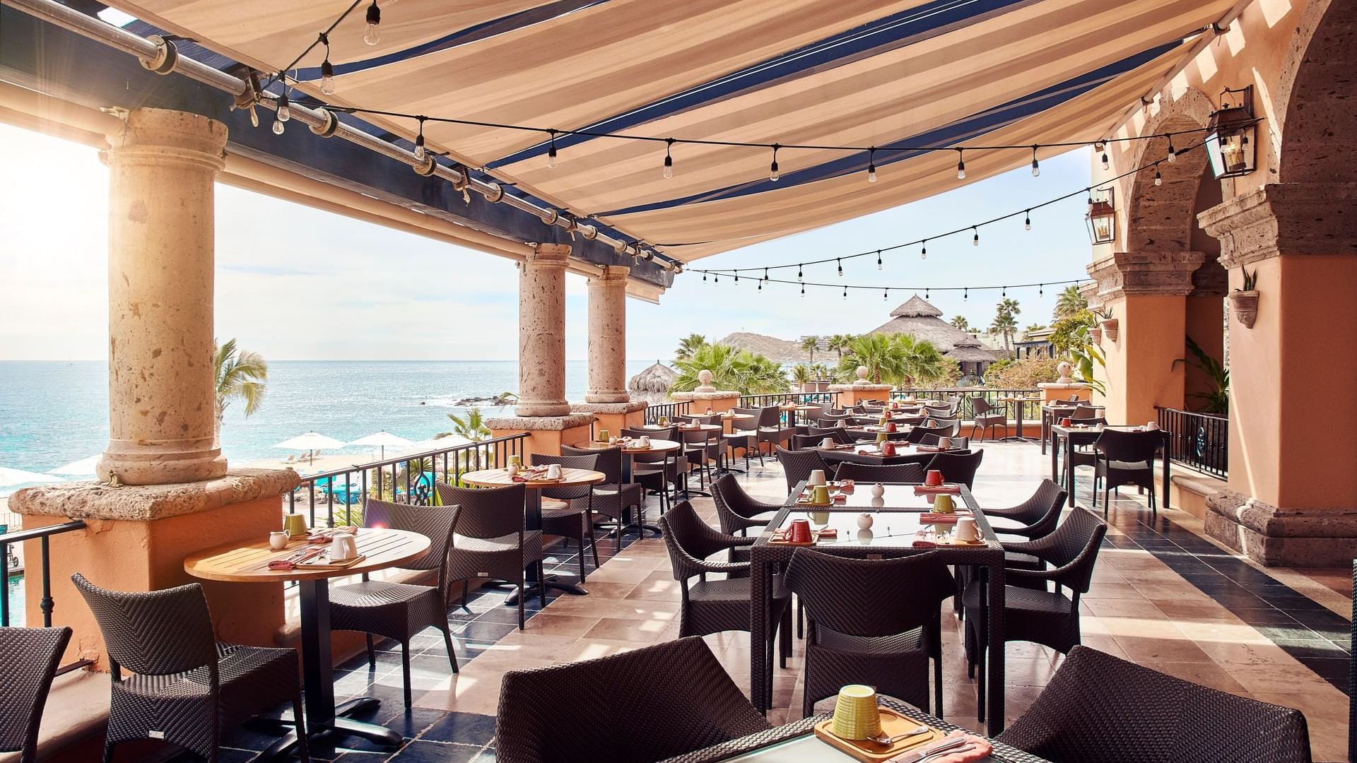 Terraza del restaurante Tomate con mesas vacías, vistas soleadas y una palapa con techo de paja en Hacienda del Mar Los Cabos.