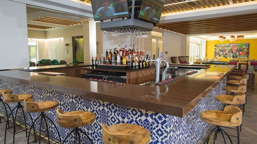 Wooden stools by a blue patterned bar and TV monitors in Rum Cay Lobby Bar at Warwick Paradise Island Bahamas